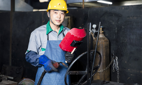 A welder is holding a red helmet