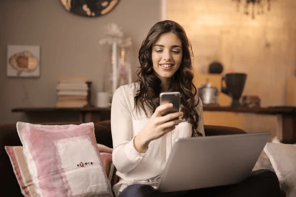 Woman Sitting on Sofa While Looking at Phone With Laptop